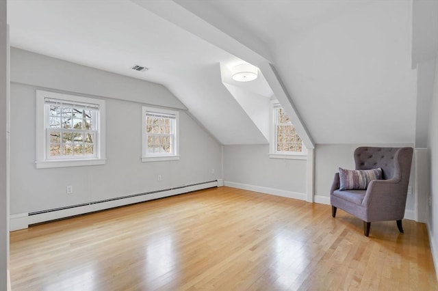 additional living space with a baseboard radiator, visible vents, wood finished floors, and vaulted ceiling