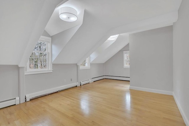 additional living space with a baseboard heating unit, baseboards, vaulted ceiling, wood finished floors, and a baseboard radiator