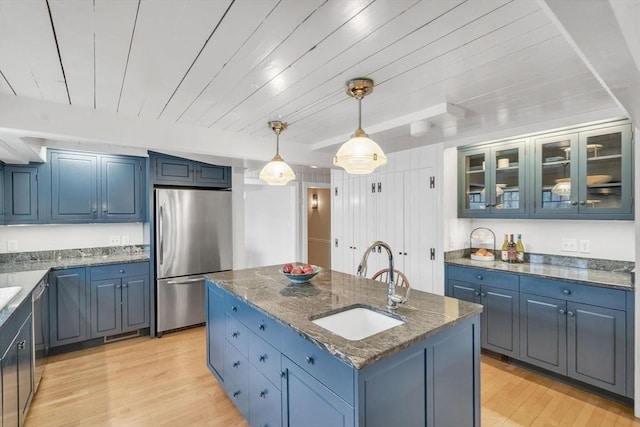 kitchen with dark stone countertops, an island with sink, a sink, appliances with stainless steel finishes, and light wood-type flooring