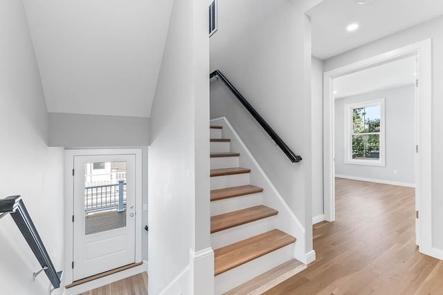 staircase featuring lofted ceiling, wood-type flooring, and a healthy amount of sunlight