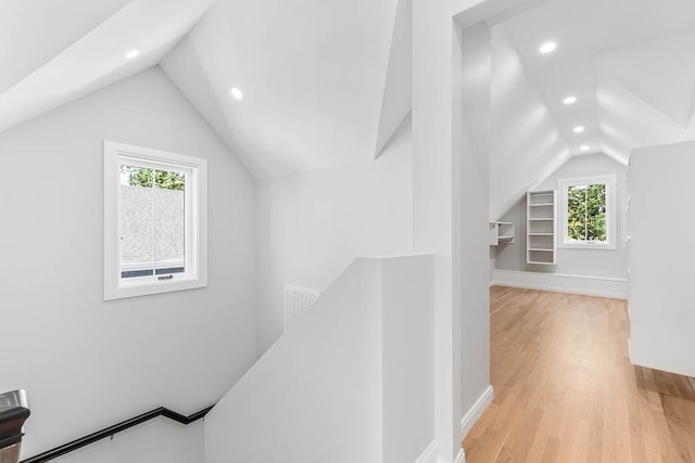 hallway featuring light wood-type flooring, vaulted ceiling, and a healthy amount of sunlight