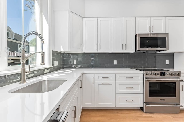 kitchen with sink, stainless steel appliances, white cabinets, and light hardwood / wood-style floors