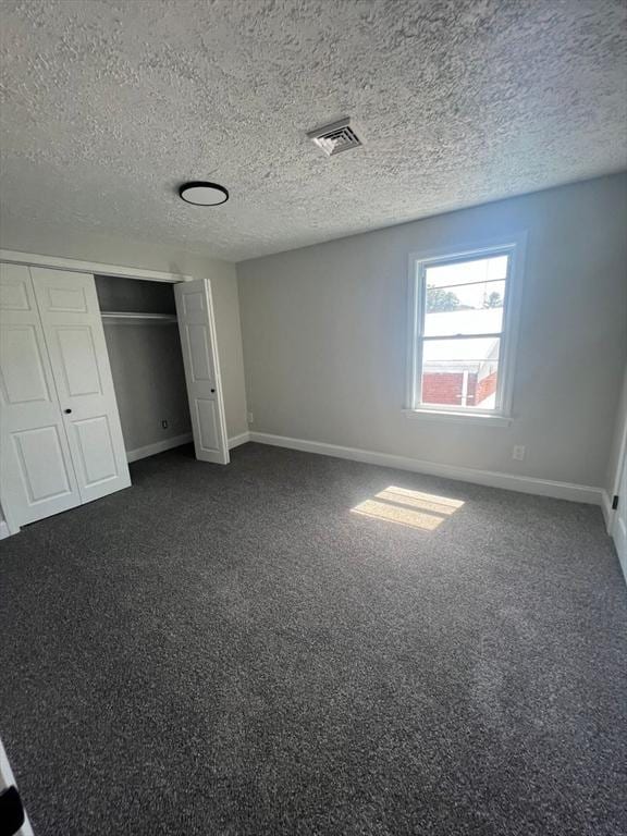 unfurnished bedroom featuring a closet, a textured ceiling, and dark colored carpet