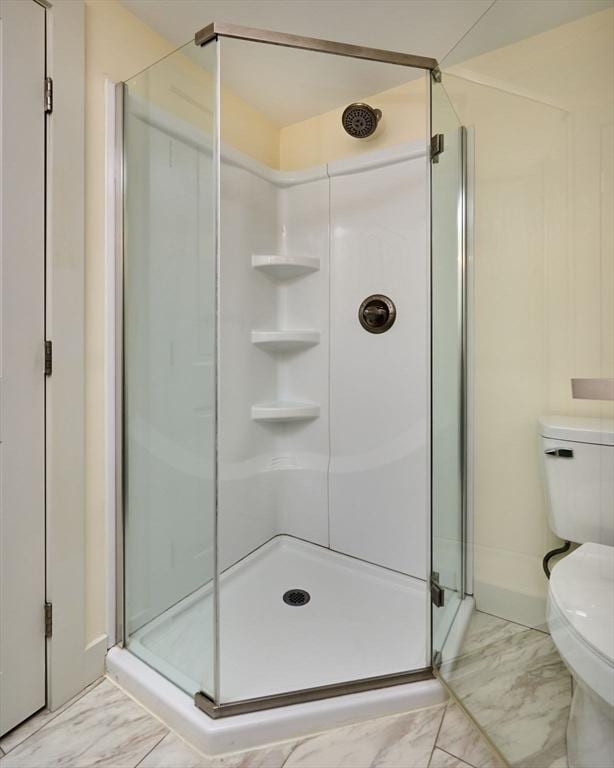 bathroom featuring toilet, marble finish floor, and a shower stall