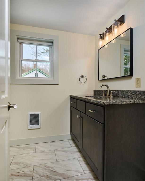 bathroom featuring heating unit, baseboards, marble finish floor, and vanity