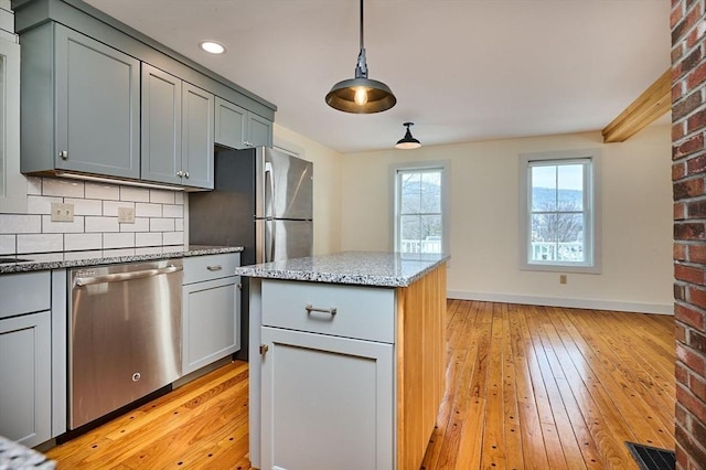 kitchen with light stone countertops, light wood-style flooring, appliances with stainless steel finishes, pendant lighting, and tasteful backsplash