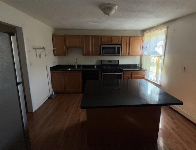 kitchen featuring sink, appliances with stainless steel finishes, a center island, a textured ceiling, and dark hardwood / wood-style flooring