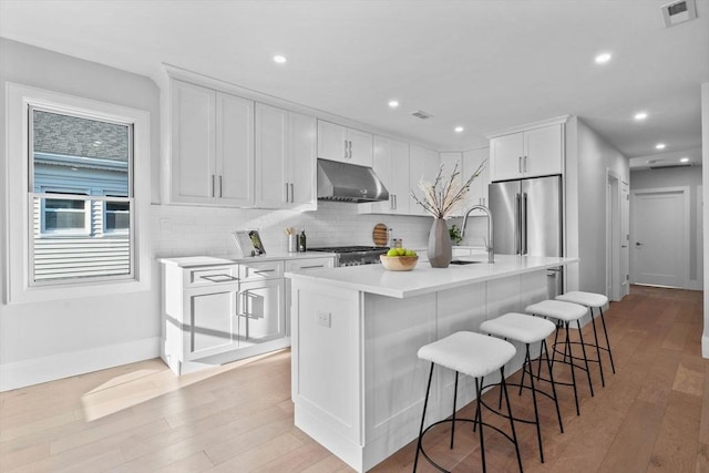 kitchen with a center island with sink, a breakfast bar, high quality fridge, white cabinets, and stove