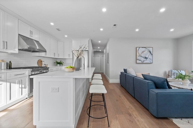 kitchen with a center island with sink, gas stove, a kitchen bar, light wood-type flooring, and white cabinetry