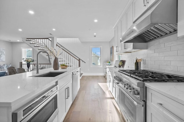 kitchen with appliances with stainless steel finishes, white cabinetry, exhaust hood, and sink