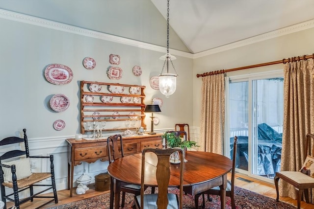 dining room with visible vents, light wood-style flooring, ornamental molding, wainscoting, and vaulted ceiling