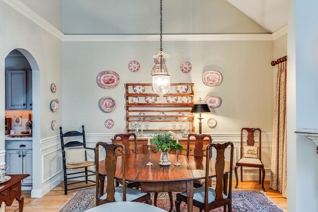 dining room with a wainscoted wall, crown molding, arched walkways, and light wood-style floors