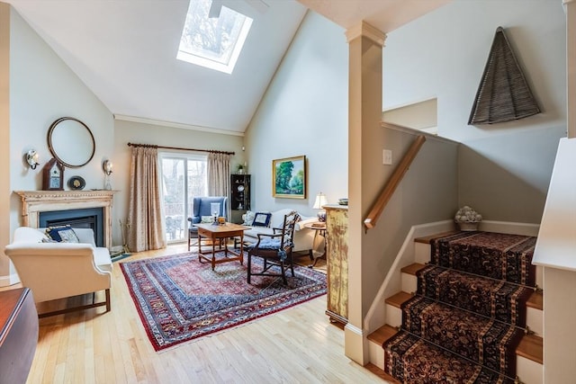 interior space featuring a skylight, baseboards, a glass covered fireplace, wood finished floors, and high vaulted ceiling