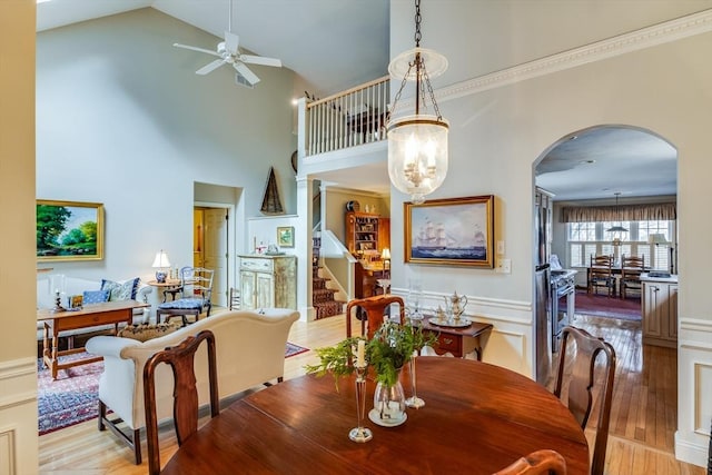 dining room featuring ceiling fan with notable chandelier, arched walkways, light wood finished floors, and stairs