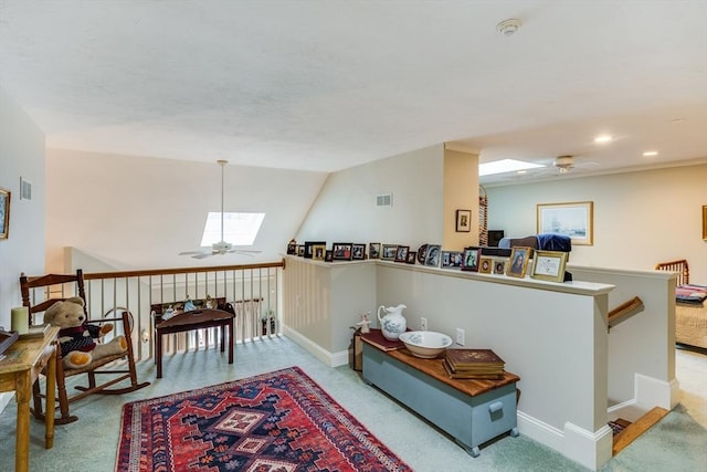 living area with lofted ceiling with skylight, light colored carpet, an upstairs landing, and a ceiling fan