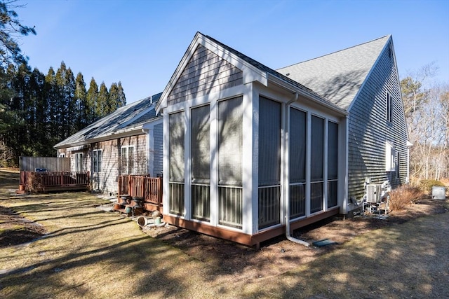 view of side of property featuring a sunroom, a shingled roof, and a deck