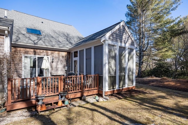 rear view of house featuring a sunroom, roof with shingles, a lawn, and a deck