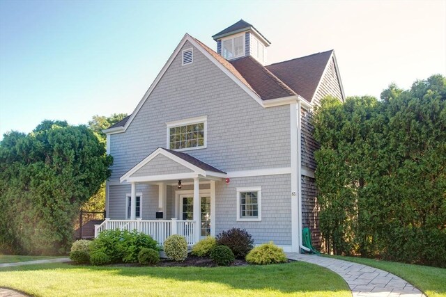 view of front of property with covered porch, a front lawn, and a shingled roof