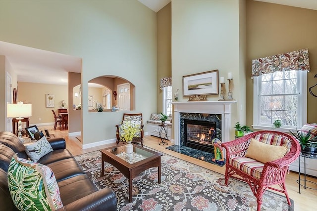 living area with baseboards, arched walkways, a towering ceiling, light wood-type flooring, and a fireplace