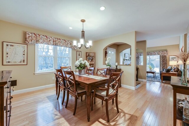 dining area with light wood-style flooring, baseboards, arched walkways, and a notable chandelier