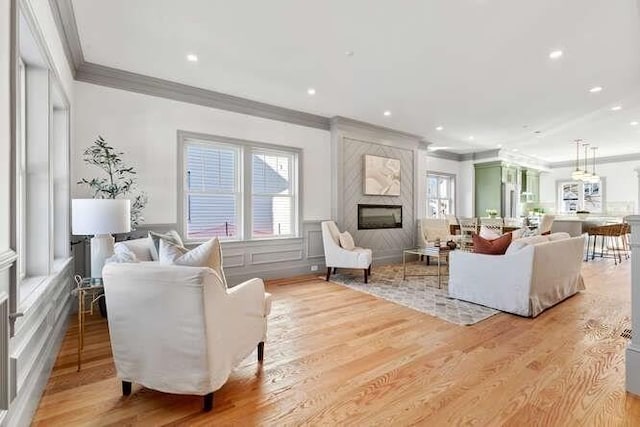 living area with a fireplace, recessed lighting, a decorative wall, ornamental molding, and light wood-type flooring