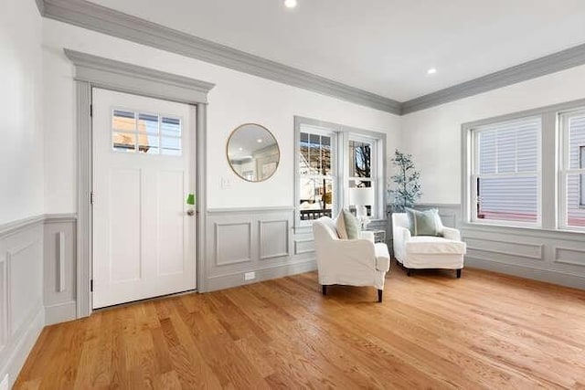 foyer entrance featuring wainscoting, crown molding, a decorative wall, and light wood finished floors