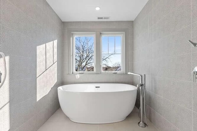 bathroom with a freestanding tub, visible vents, and tile walls