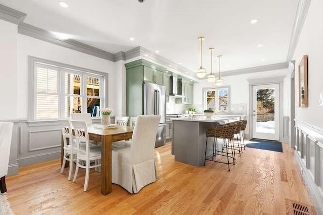 dining area featuring ornamental molding, wainscoting, a decorative wall, and light wood-style flooring