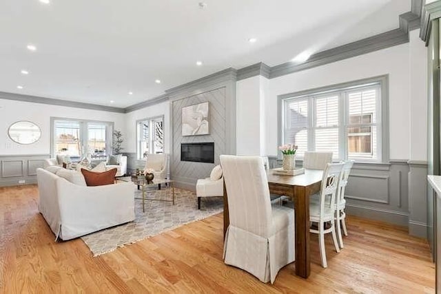 dining space with light wood-style floors, ornamental molding, a decorative wall, and a high end fireplace