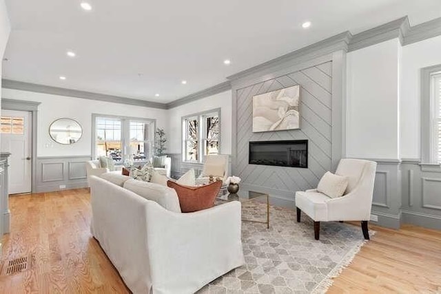 living room with recessed lighting, a decorative wall, a fireplace, light wood-type flooring, and crown molding