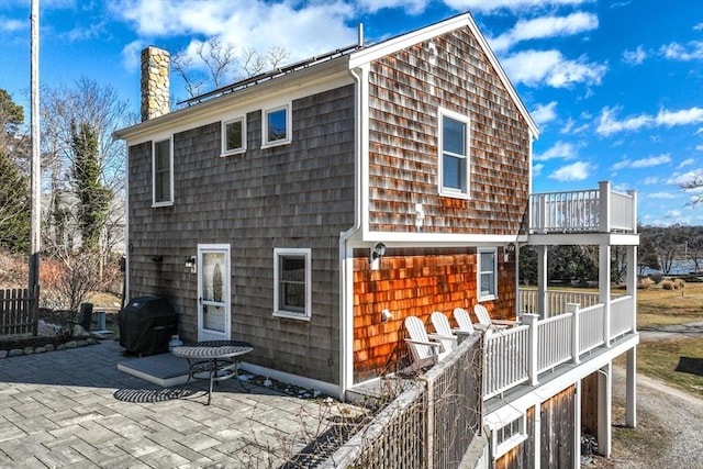 rear view of house with a balcony, a chimney, and a patio