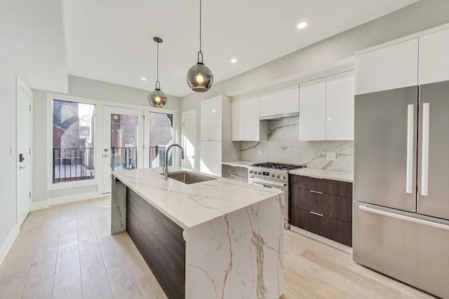 kitchen with appliances with stainless steel finishes, an island with sink, light stone counters, white cabinets, and sink