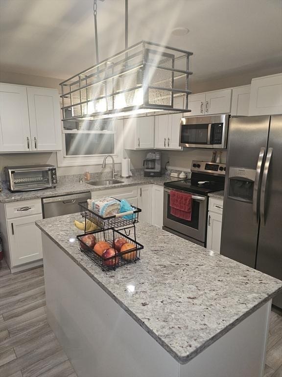 kitchen featuring sink, appliances with stainless steel finishes, white cabinetry, hardwood / wood-style floors, and light stone counters