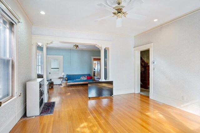 living room with a wealth of natural light, wood finished floors, decorative columns, and a ceiling fan