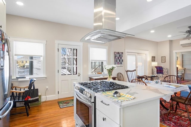 kitchen with light stone counters, island range hood, white cabinetry, appliances with stainless steel finishes, and a wall mounted air conditioner