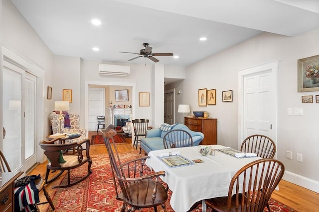 dining area featuring a ceiling fan, wood finished floors, a wall mounted AC, a fireplace, and recessed lighting