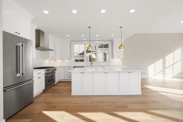 kitchen with a kitchen island, decorative light fixtures, white cabinets, premium appliances, and wall chimney exhaust hood