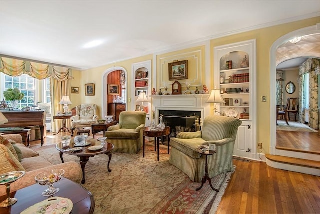 living area with built in shelves, light hardwood / wood-style floors, and crown molding