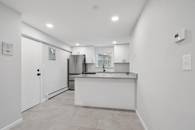 kitchen with stainless steel fridge, light stone countertops, baseboard heating, tasteful backsplash, and white cabinetry