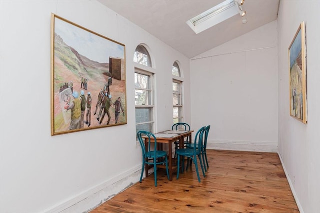 dining space featuring hardwood / wood-style floors and vaulted ceiling with skylight