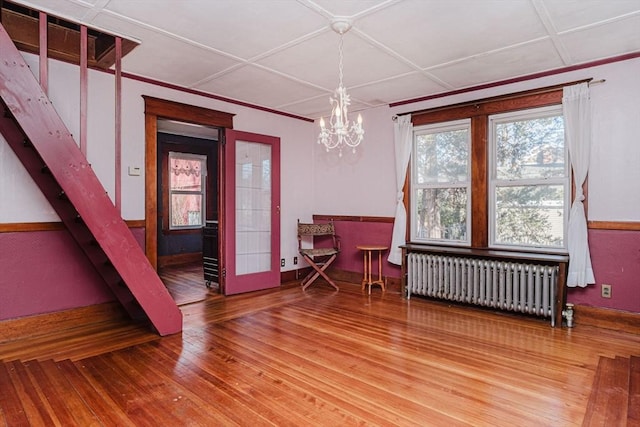 dining area featuring radiator heating unit, wood-type flooring, coffered ceiling, and an inviting chandelier