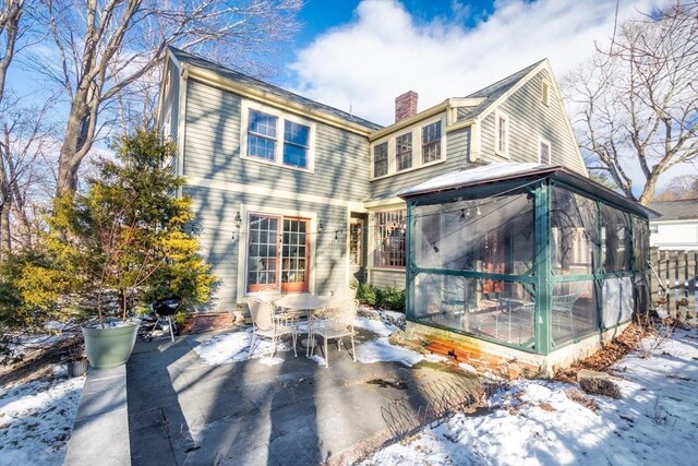 snow covered back of property with a patio area and a sunroom