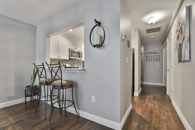 hallway featuring baseboards, visible vents, and dark wood-style flooring