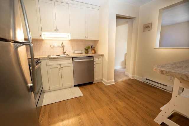 kitchen with appliances with stainless steel finishes, a sink, baseboard heating, decorative backsplash, and light wood-type flooring
