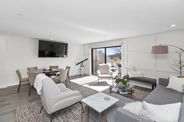 living room with recessed lighting, a decorative wall, baseboards, and wood finished floors