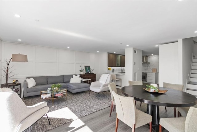 living room with a decorative wall, light wood-style flooring, recessed lighting, and stairs
