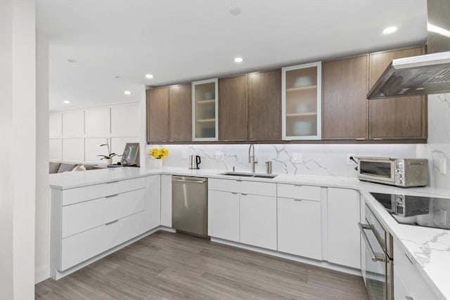 kitchen with a sink, wall chimney range hood, appliances with stainless steel finishes, a peninsula, and light wood-style floors