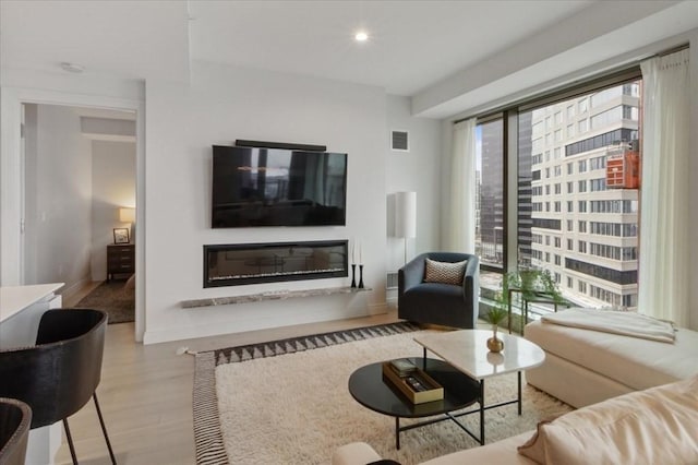 living area with a glass covered fireplace, visible vents, wood finished floors, and recessed lighting