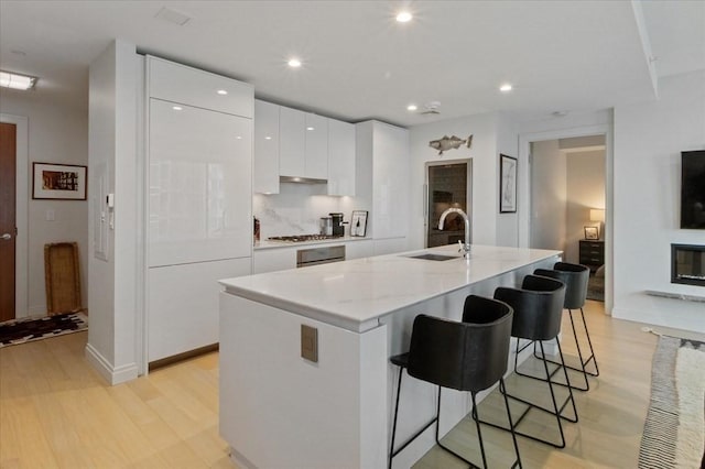 kitchen featuring a sink, a center island with sink, a breakfast bar area, white cabinetry, and modern cabinets