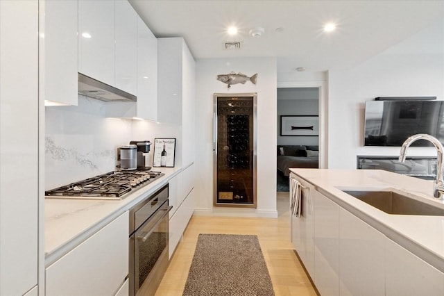 kitchen featuring under cabinet range hood, appliances with stainless steel finishes, white cabinets, modern cabinets, and a sink